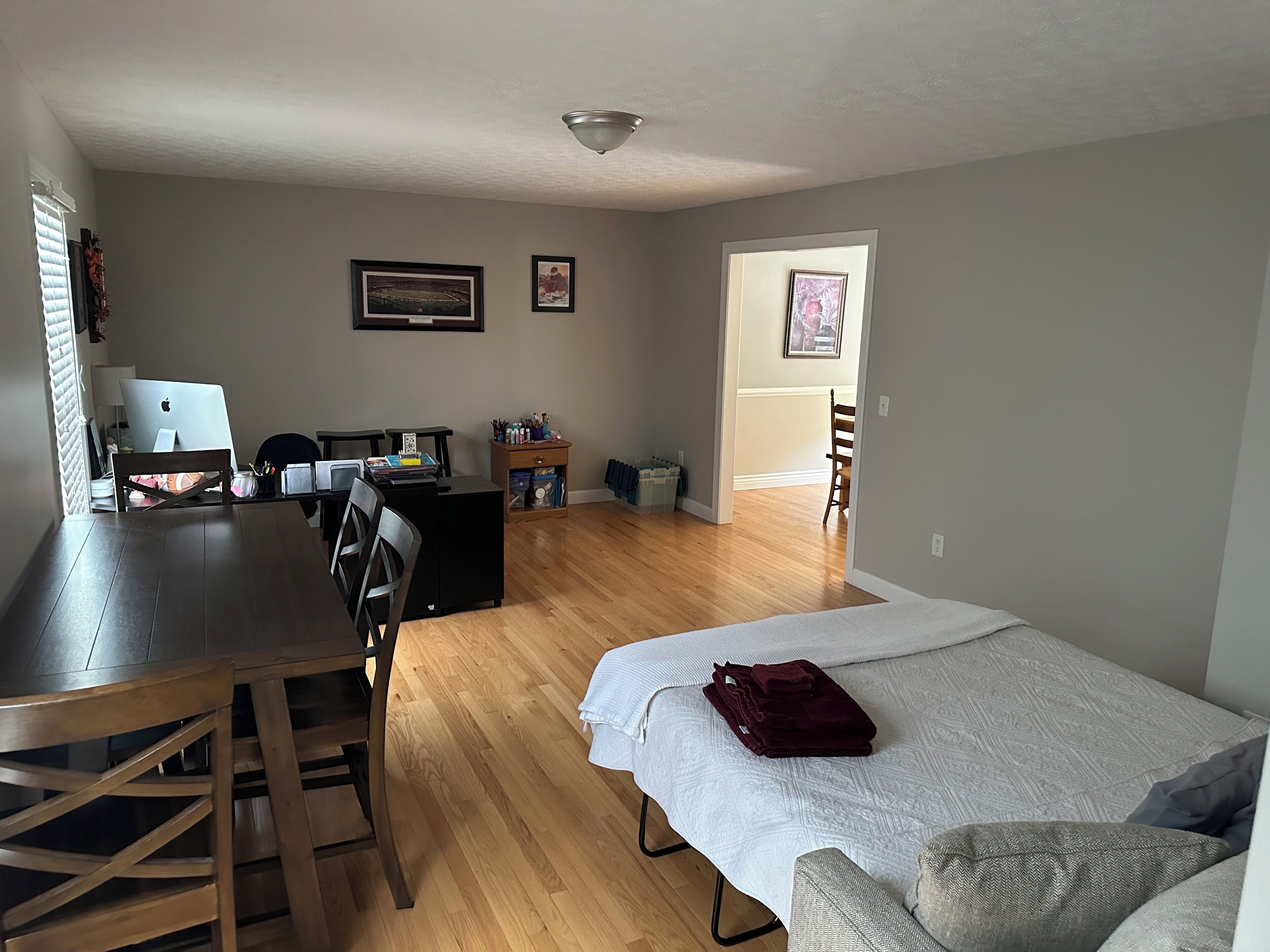 A room with a bed, a desk with a laptop, a chair, and a small table with various items.