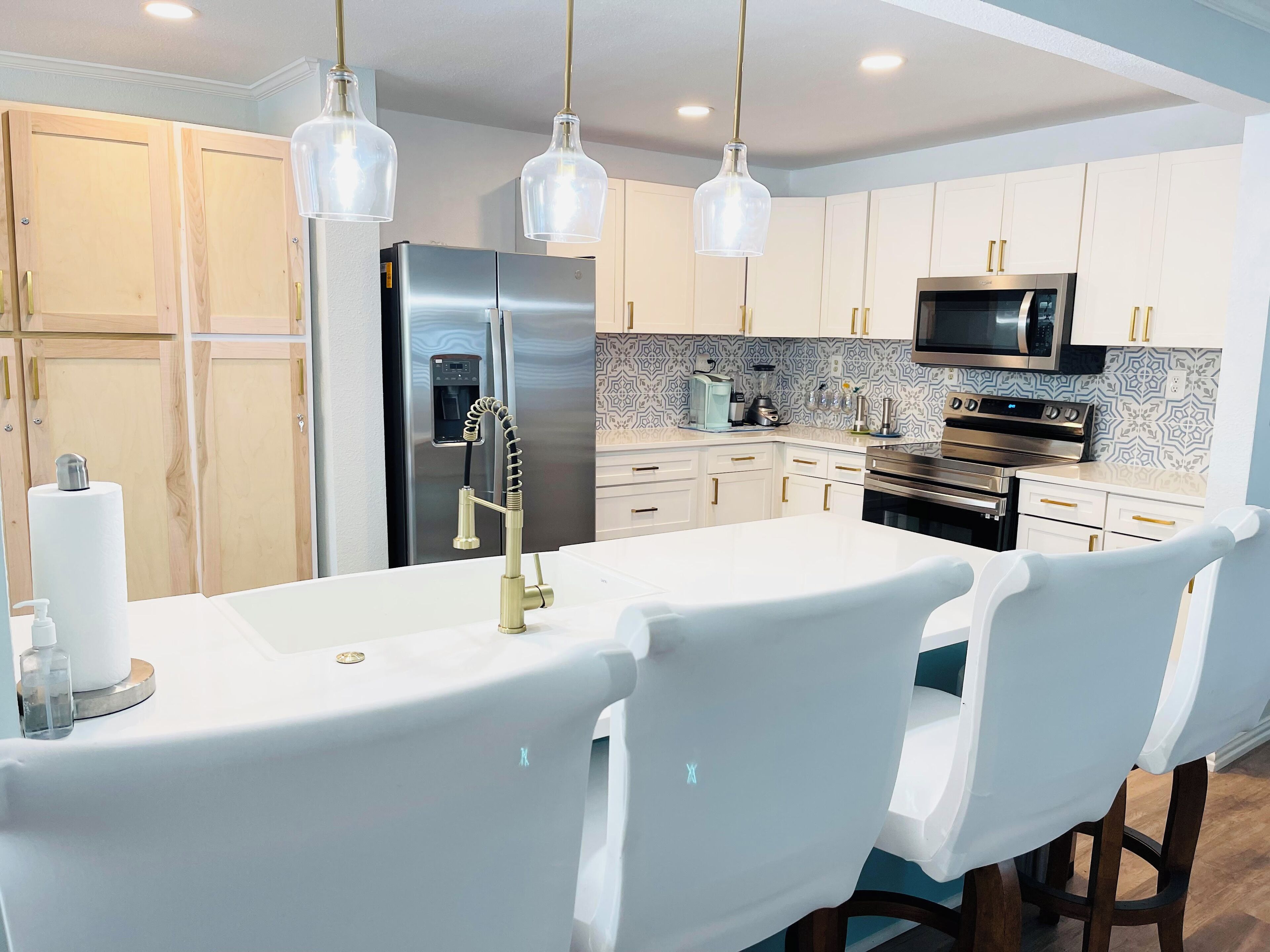 A modern kitchen with white cabinetry, stainless steel appliances, and pendant lighting.