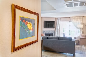 Ein gerahmtes Kunstwerk an der Wand, ein graues Sofa und ein Flachbildfernseher in einem Wohnzimmer.