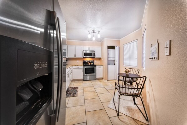 A compact kitchen with a refrigerator, microwave, oven, and sink. There is a dining area with a table and chairs. - The Cactus Flower at McCormick Ranch (Scottsdale)