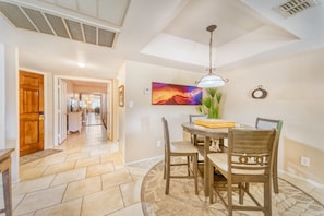 A dining area with a round table, chairs, a hanging light fixture, and a painting on the wall.