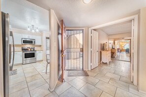 A modern kitchen with stainless steel appliances, a dining area with a wooden table, and a view of the living room through an open door. - The Cactus Flower at McCormick Ranch (Scottsdale)