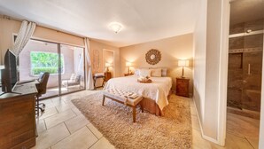A bedroom with a large bed, a desk, a chair, a bench, and a shower area. - The Cactus Flower at McCormick Ranch (Scottsdale)