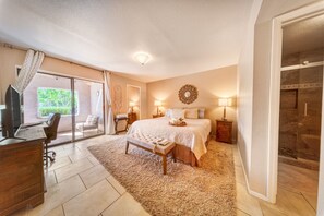 A bedroom with a bed, bedside tables, a desk, and a large window.