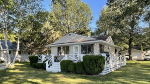 A single-story house with a white exterior, a porch with white railings, and a small front yard with trimmed bushes. - Lake Frontage, swimming area, close to golf (Markesan)