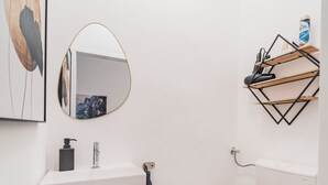 A modern bathroom with a white sink, a round mirror, a toilet, and a shelf with toiletries. - 3 Bedrooms - 75sqm - 15 Min. City Center (Vienna)