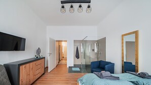 A modern bedroom with a bed, a TV, a wooden cabinet, a blue chair, and a large mirror. - 3 Bedrooms - 75sqm - 15 Min. City Center (Vienna)