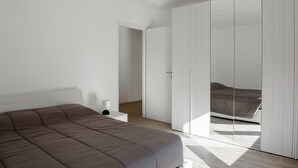A modern bedroom with a large bed, a bedside table, a wardrobe, and a door leading to another room. - Chalet Francesca (Pieve di Cadore)