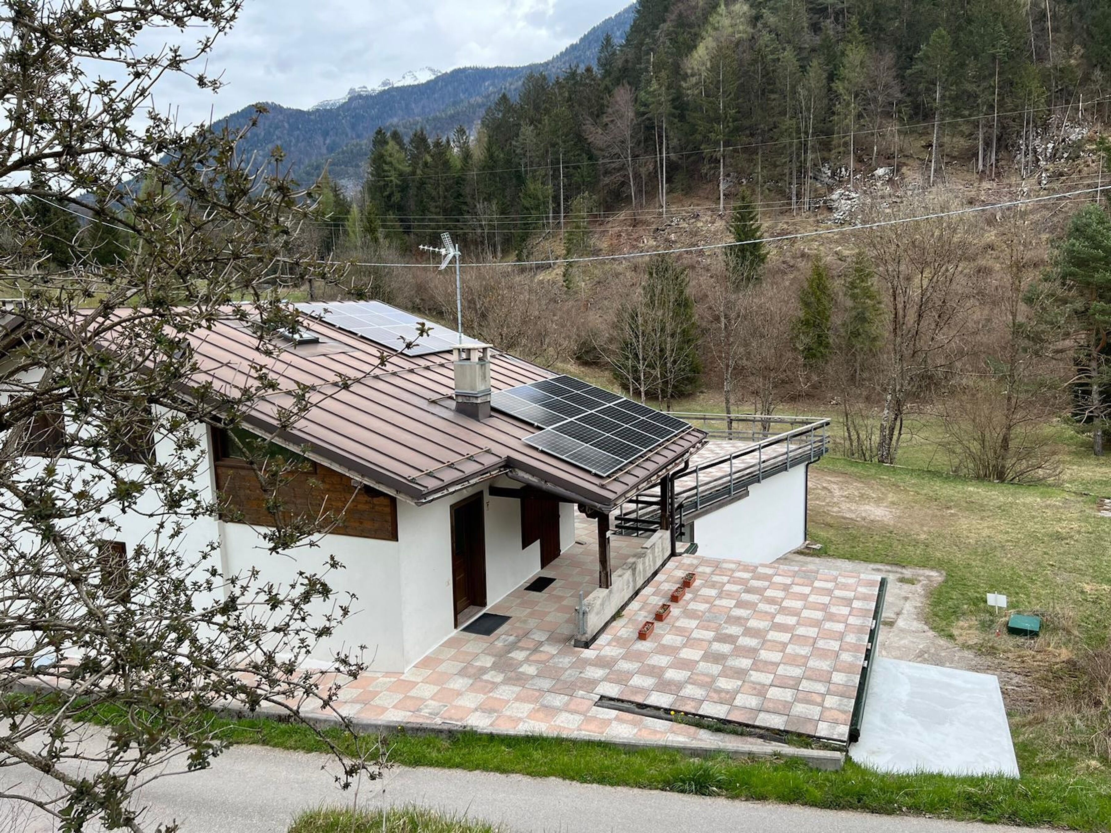 Een modern huis met een dak voorzien van zonnepanelen, een overdekt terras en uitzicht op een bebost berglandschap.