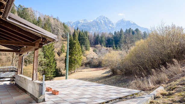 A covered outdoor area with a view of snow-capped mountains, a wooden pergola, and a paved patio. - Chalet Francesca (Pieve di Cadore)