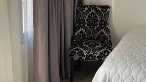 Una habitación con cama, una silla y una ventana con cortinas.