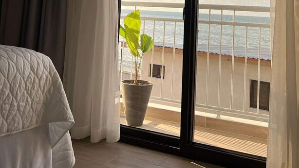 Una habitación de hotel con cama, una planta en maceta y un balcón con vista al mar.