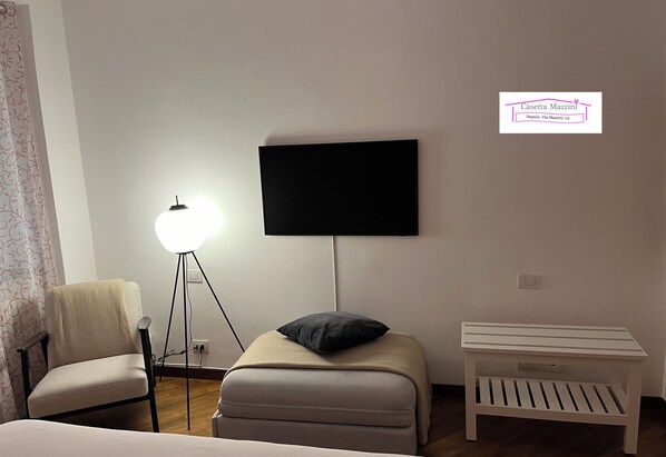A bedroom with a bed, a chair, a bedside table, a lamp, and a TV mounted on the wall.