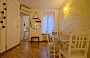 A room with a wooden floor, a dining table with chairs, a mirror on the wall, and a window with curtains.