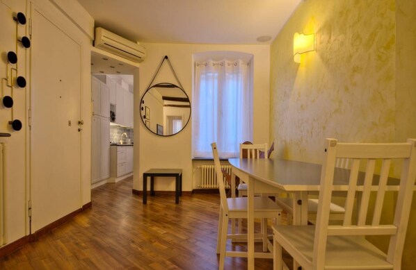 A room with a wooden floor, a dining table with chairs, a mirror on the wall, and a window with curtains.