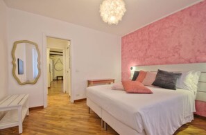 A bedroom with a bed, bedside tables, a mirror, and a pink accent wall.