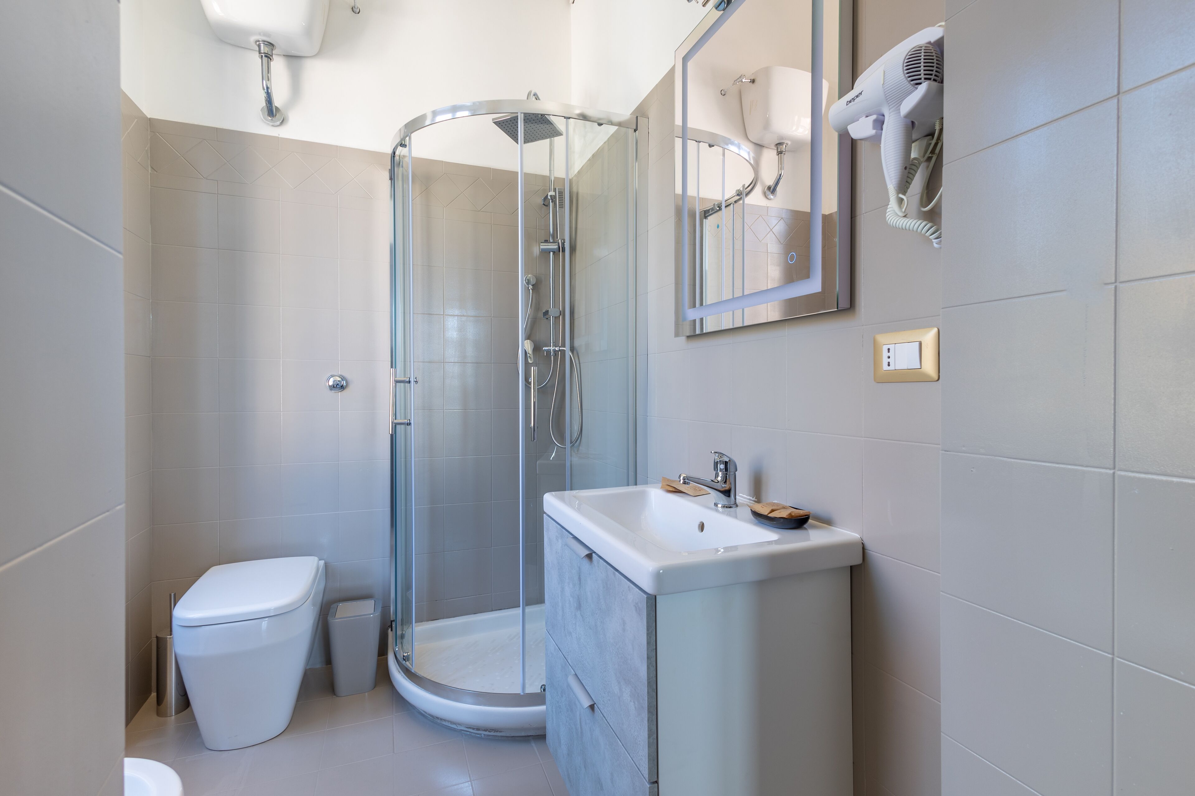 Un baño moderno con ducha de vidrio, inodoro blanco y tocador con espejo.