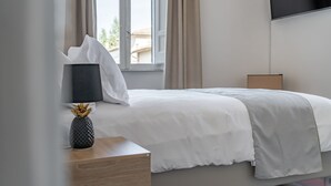 A neatly made bed with white bedding, a bedside table with a vase, and a TV mounted on the wall. - Palazzo Dasso (Viterbo)