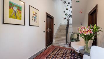Un couloir orné de tableaux encadrés, un escalier, un tapis à motifs et un vase rempli de fleurs.