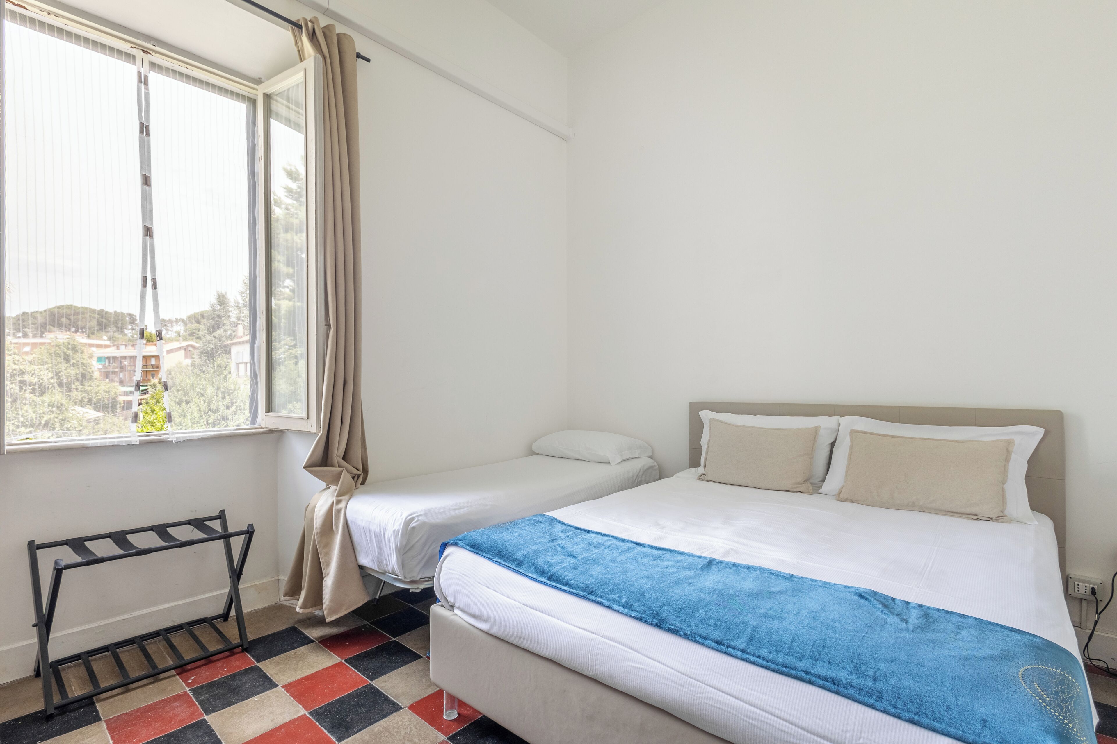 A hotel room with two beds, a window with curtains, a radiator, and a checkered floor.