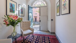 A hallway with framed artwork, a vase of flowers, a chair, and a patterned rug. - Palazzo Dasso (Viterbo)