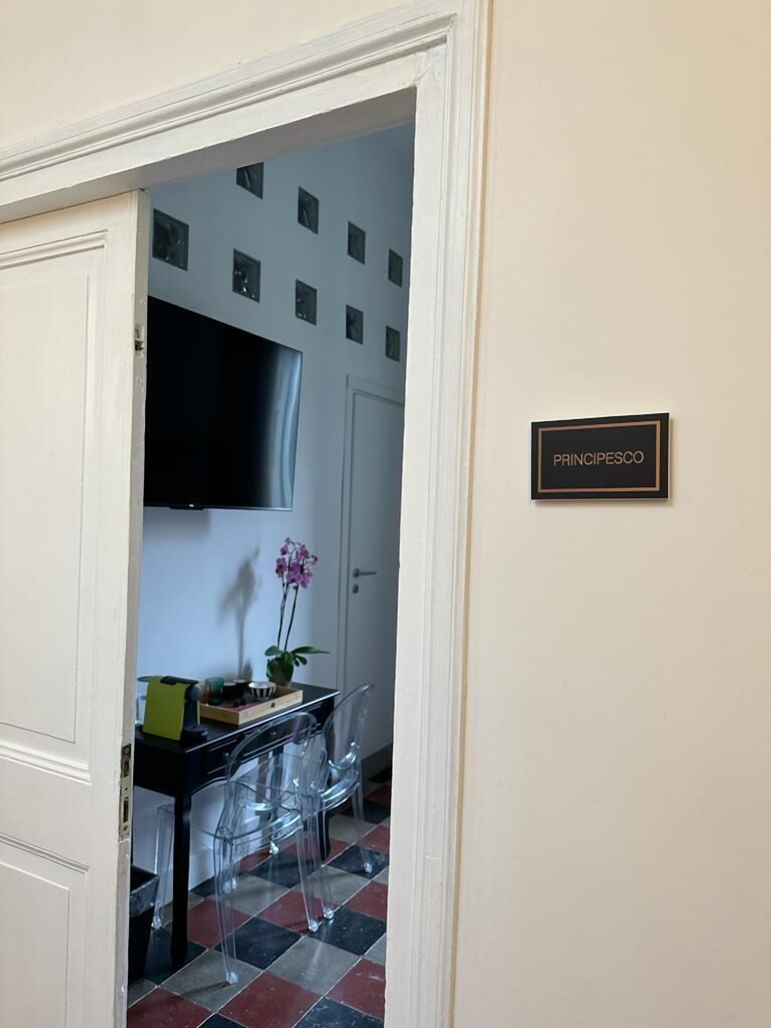 Ett hotellrum med en matplats som har ett svart bord, genomskinliga stolar och en orkidé i en kruka. En tv är monterad på väggen ovanför bordet.