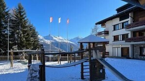 A snow-covered playground with a slide and climbing structure, surrounded by trees and a mountain in the background. - Cosy studio for 5 near ski lift, Les Gentianes (Les Collons)