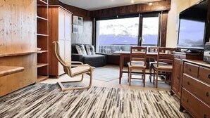 A modern interior with a wooden floor, a dining area with chairs and a table, a sofa, and a large window with a mountain view. - Cosy studio for 5 near ski lift, Les Gentianes (Les Collons)