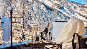 Ein Tisch mit einer Champagnerflasche, zwei Gläsern und einer Serviertschale vor einer verschneiten Berglandschaft.
