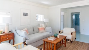 A modern living room with a grey sofa, a wooden coffee table, and a white armchair. There is a wooden side table with a lamp and a vase. - Palmetto Bungalow - Quaint, original Fairhope cottage close to town. (Fairhope)