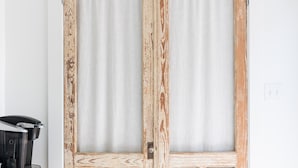 A room with a wooden door with glass panels, a wooden dresser, and a light-colored floor. - Palmetto Bungalow - Quaint, original Fairhope cottage close to town. (Fairhope)