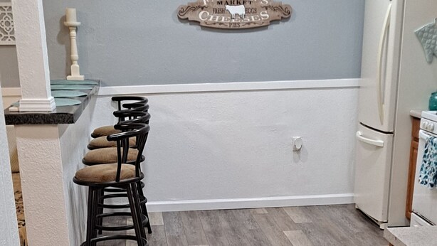 Una cocina moderna con piso de madera, un comedor con sillas y un refrigerador.