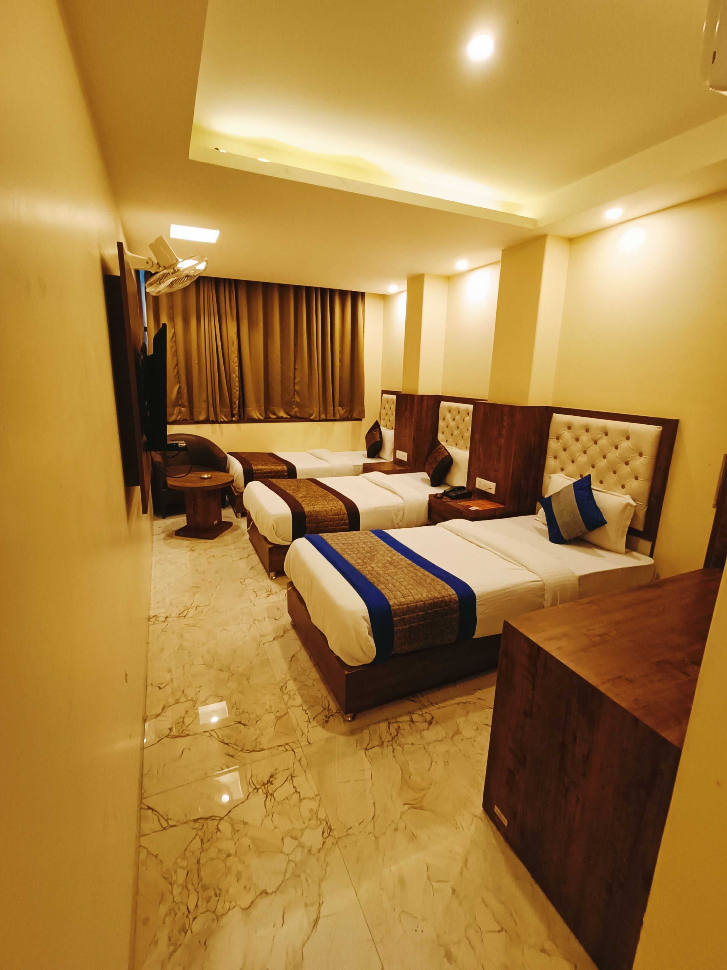 A hotel room with three beds, a wooden headboard, a marble floor, and a ceiling fan.