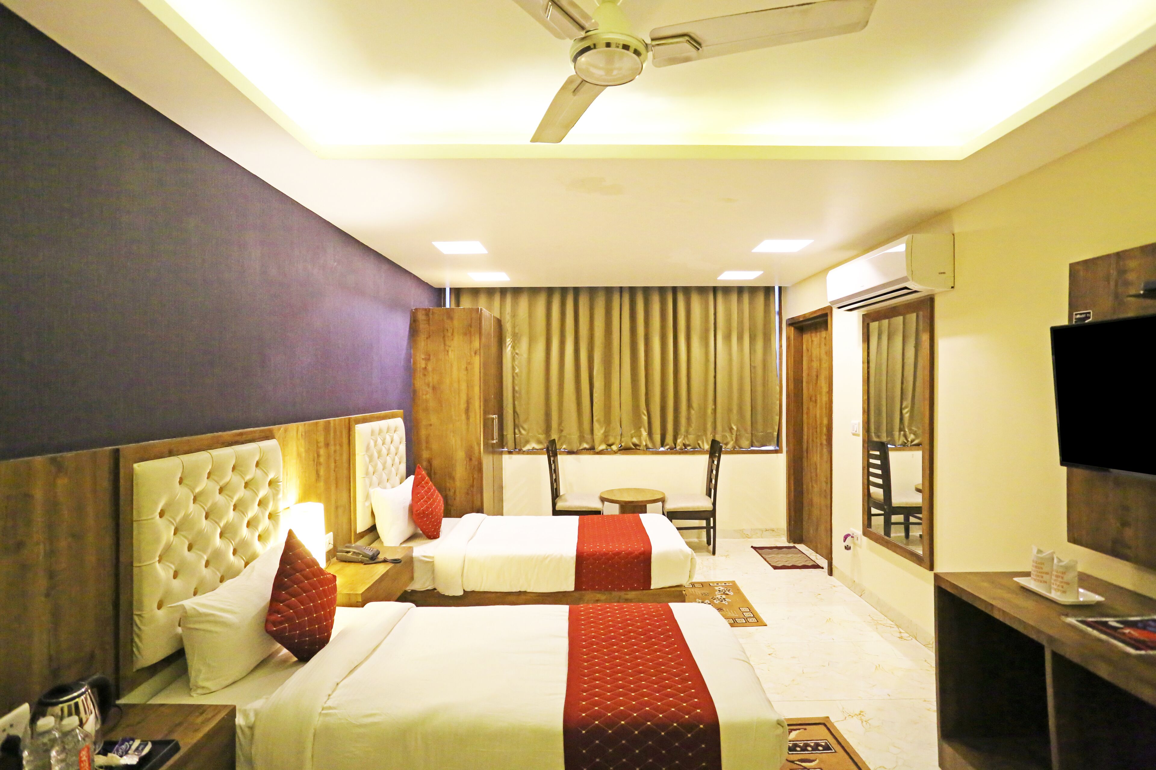 A hotel room with two beds, a ceiling fan, a TV, and a small table.