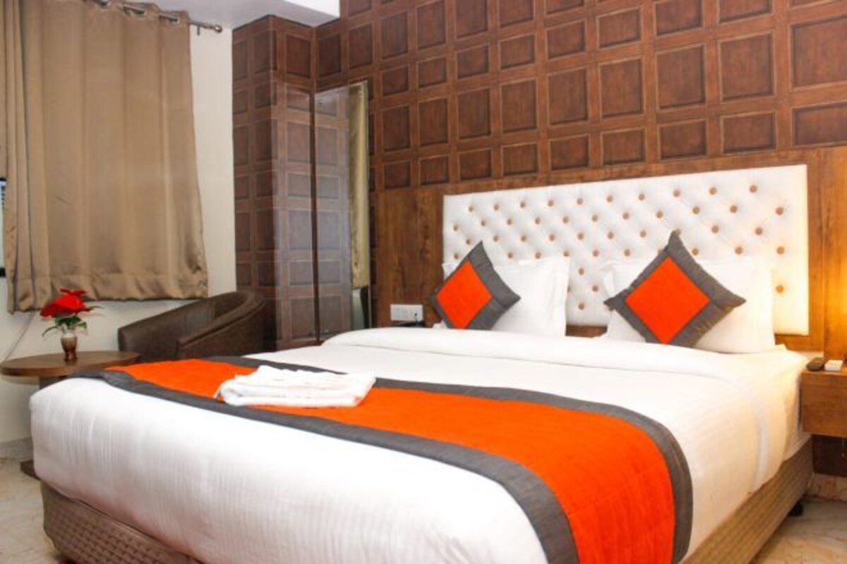 A hotel room with a large bed, wooden panel walls, a nightstand, and a vase with a red flower.
