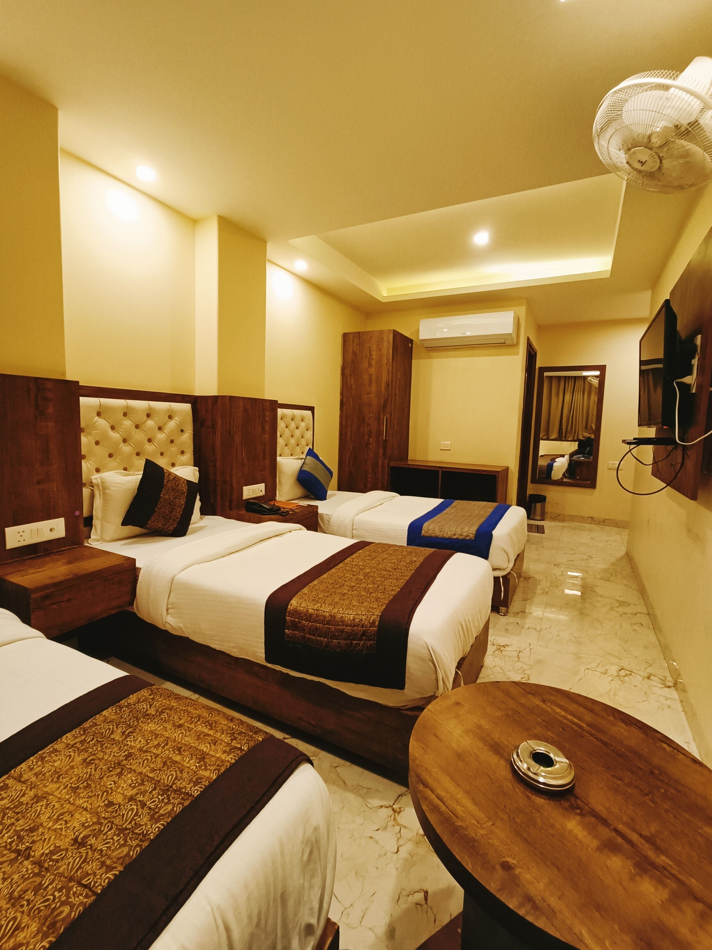 A hotel room with three beds, wooden headboards, a marble floor, and a TV mounted on the wall.