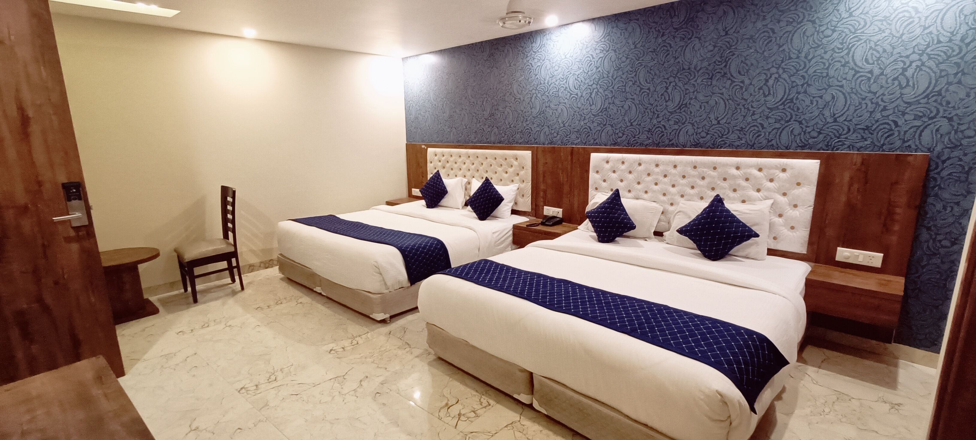 A hotel room with two beds, marble flooring, a wooden headboard, and a patterned wall.