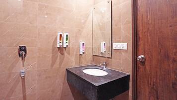 A bathroom with a marble wall, a sink with a mirror, and two soap dispensers.