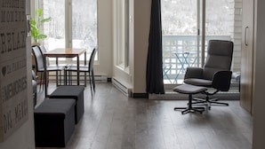 A room with a dining table, chairs, a bench, a large window with a view, and a chair by the window. - Loft Ski-in/Ski-out Stoneham resort (Stoneham-et-Tewkesbury)