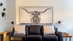 A modern living room with a black leather sofa, two matching ottomans, a large bull-themed painting on the wall, and a small side table with a lamp. - Loft Ski-in/Ski-out Stoneham resort (Stoneham-et-Tewkesbury)