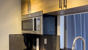 A modern kitchen with wooden cabinets, a built-in microwave, a coffee machine, and a stainless steel sink. - Loft Ski-in/Ski-out Stoneham resort (Stoneham-et-Tewkesbury)