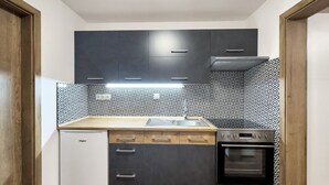 A compact kitchen with dark cabinets, a white refrigerator, a patterned backsplash, and a built-in oven.