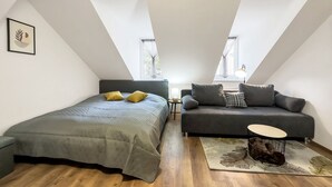 A loft bedroom with a bed, a sofa, a small table, and a window.