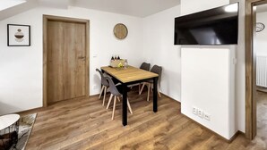 A dining area with a wooden table, chairs, a clock, and a TV mounted on the wall.