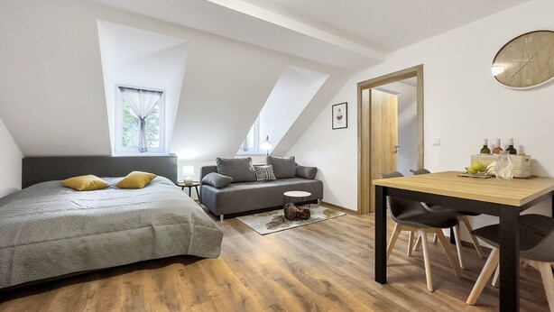 A modern loft bedroom with a large bed, a sofa, a dining table, and a wooden floor.