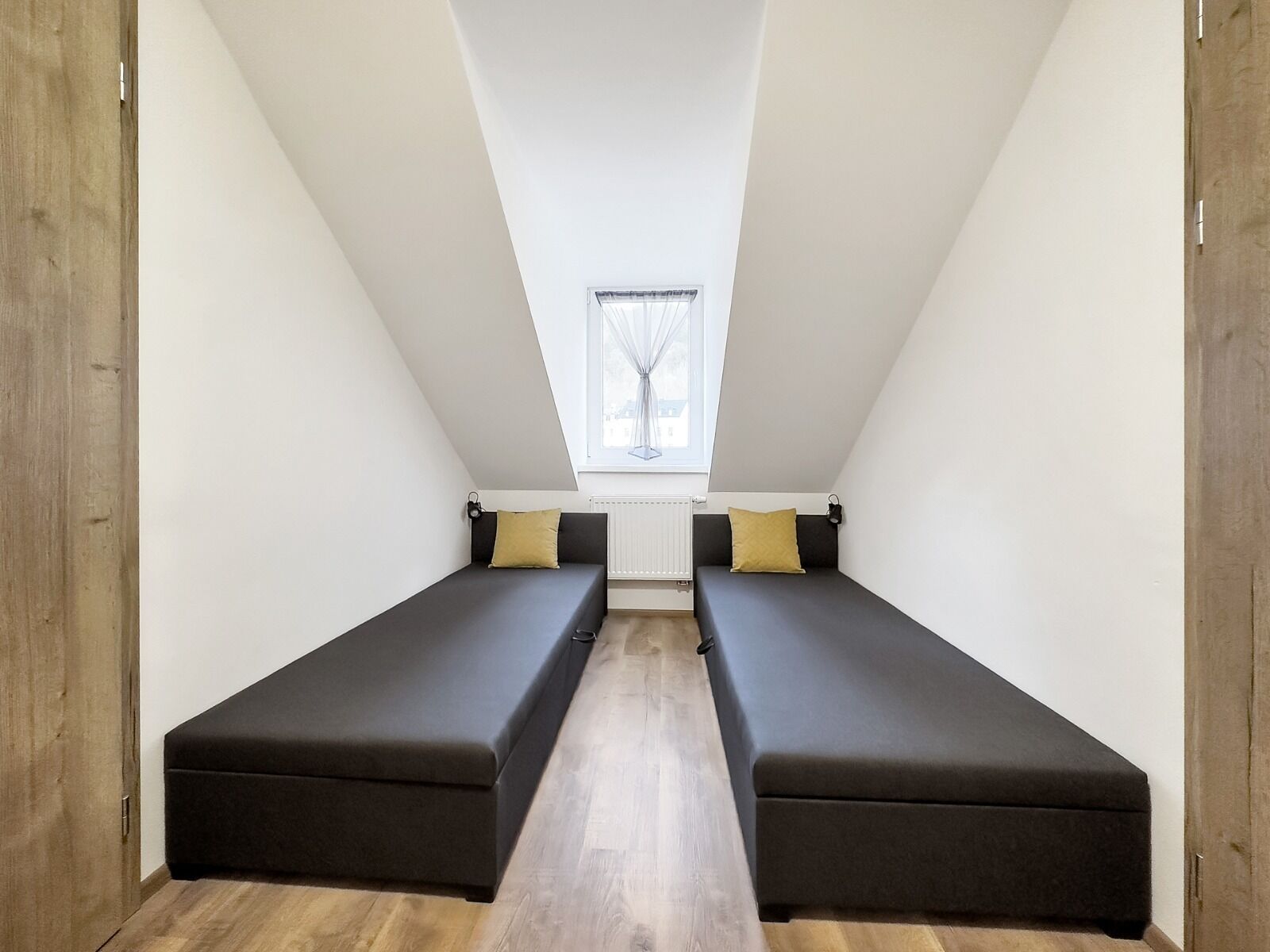Una habitación pequeña y moderna con dos camas individuales, una ventana y un techo inclinado.