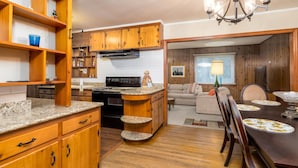 Una cocina con armarios de madera, encimeras de granito y una isla central. Hay una zona de comedor con una mesa y sillas de madera.