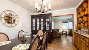 Un comedor con una mesa de madera oscura, sillas y una araña. Se observa un aparador con puertas de vidrio y un espejo en la pared.