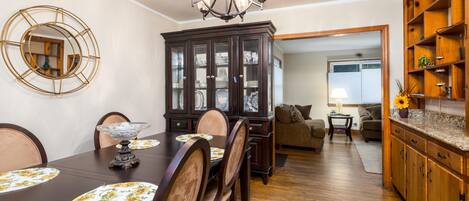 A dining area with a dark wooden table, chairs, and a chandelier. There is a cabinet with glass doors and a mirror on the wall.