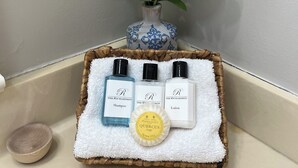A bathroom vanity with a white towel, a small vase with a purple flower, and three bottles of The Richardson brand toiletries.